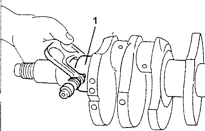 Hand holding a tool against a crankshaft with numbered part 1 pointing to the journal area.