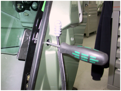 A screwdriver being used to remove a screw from the top edge of a car door glass.