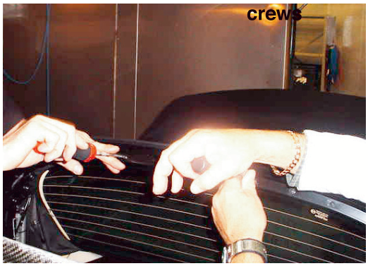 A pair of hands using a screwdriver to remove screws from the roof lining near the tension bow.