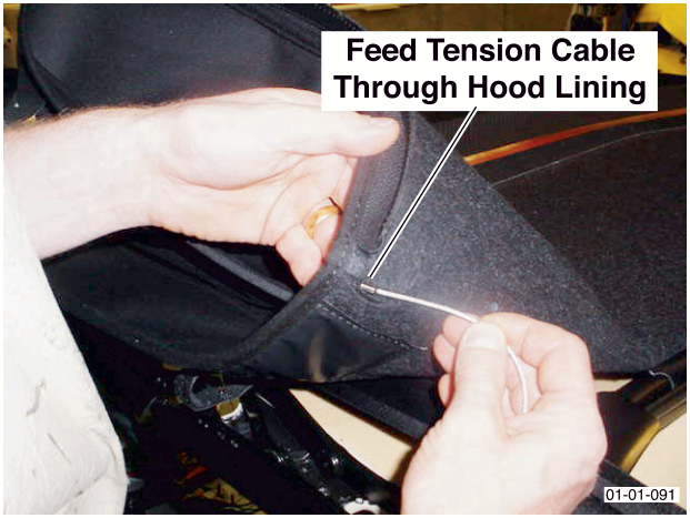 A hand feeding a thin white tension cable through an opening in the black hood lining. Label reads Feed Tension Cable Through Hood Lining.