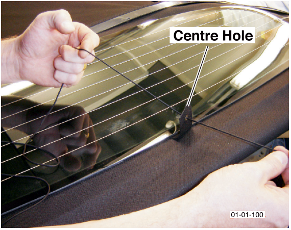 A hand threading a thin tension cord through a centre hole in the roof material near the rear window.
