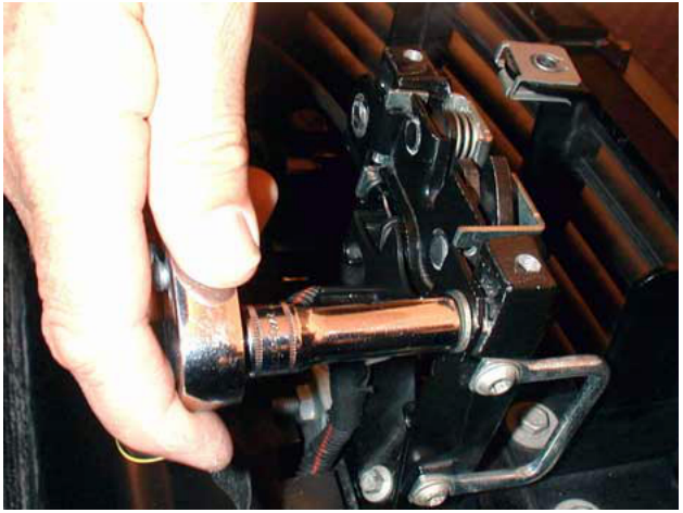 Photograph of a hand using a ratchet wrench to remove a bolt securing a component in the engine bay