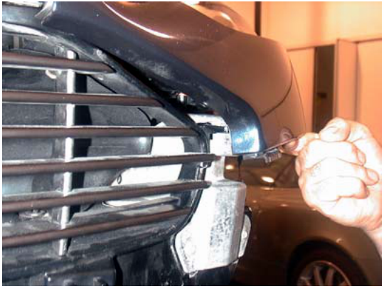 A hand removing a wing from the front grill area of a vehicle