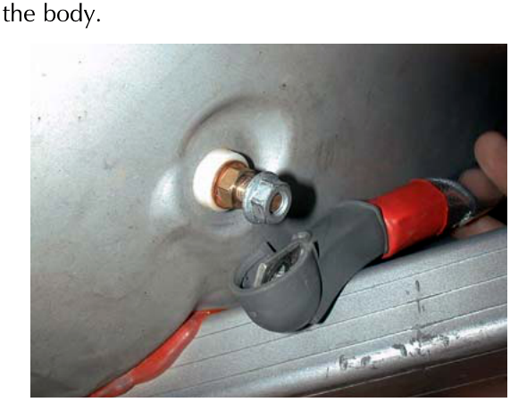 A close-up photograph of a red insulated cable connected to a bolted earth point on the vehicle body metalwork.