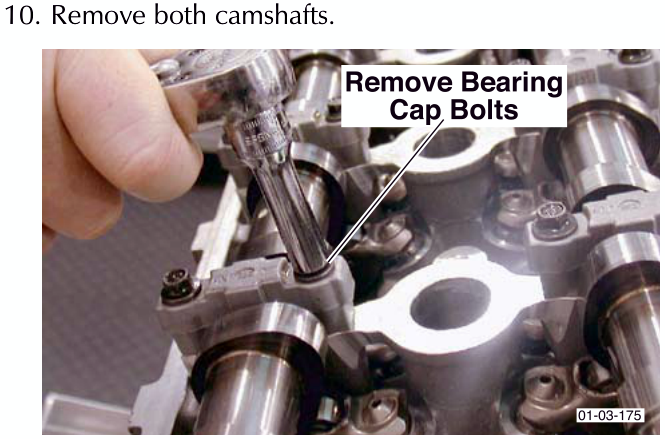 A hand using a tool to remove bearing cap bolts from the cylinder head assembly.