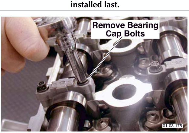 Close-up photograph of hands removing bearing cap bolts from the camshaft assembly.