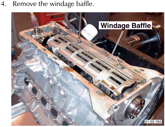 A photograph of an engine block showing the windage baffle being removed. The label 'Windage Baffle' points to the component.