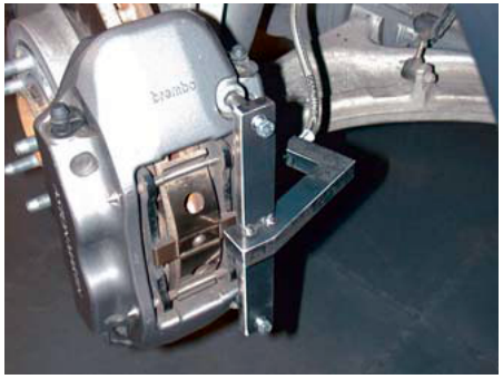 Close-up photograph of a brake caliper with a metal alignment tool installed on the brake pipe union