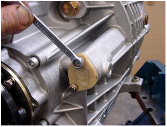 Close-up photograph of a hand using a wrench to remove a bolt from the differential housing, next to a yellow gauze filter.