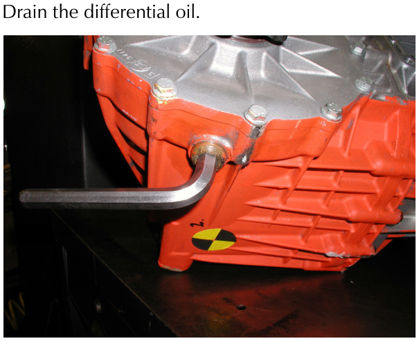 A metal drain plug being removed from the bottom of an orange differential housing using a wrench.
