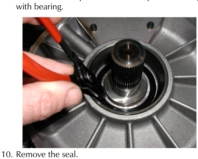 A hand using red-handled pliers to remove a circlip from around the splined output shaft inside the differential housing.