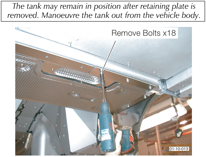 View from underneath showing a hand using a power tool to remove bolts from a metal retaining plate across the bottom of the fuel tank. Callout reads 'Remove Bolts x18'