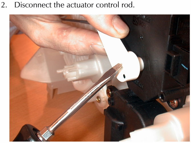 Close-up photo of a hand using a tool to disconnect the white plastic actuator control rod from the black actuator housing