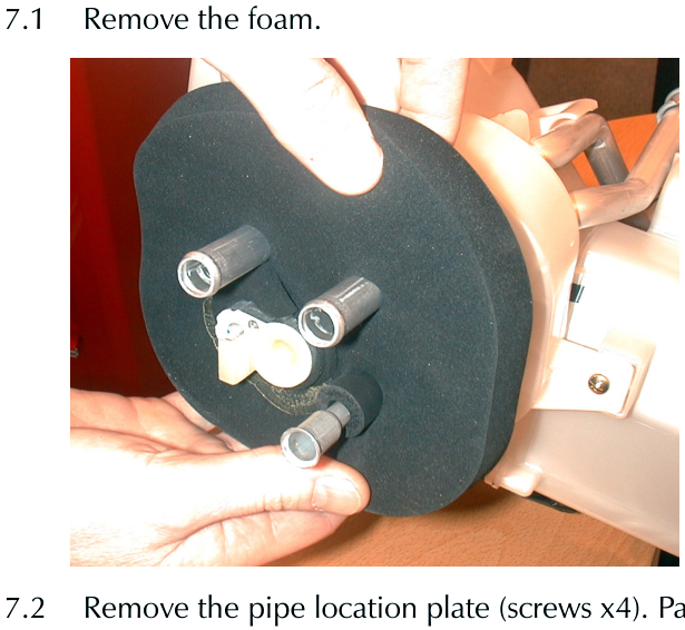 Hand removing a circular black foam component from a white plastic housing with three protruding metal pipes.
