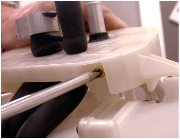 Close-up of a screwdriver removing a screw from a white plastic pipe location plate.