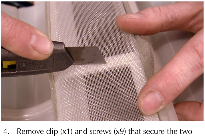 A hand using a utility knife to cut through filter gauze and foam inside the A/C unit housing.