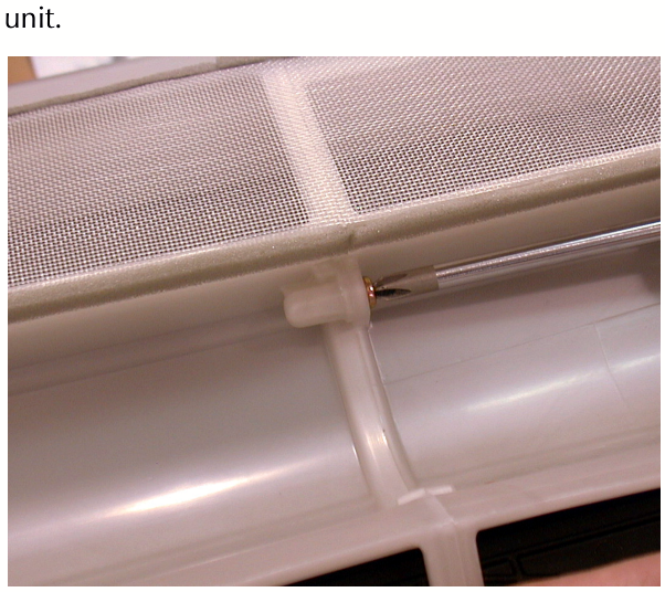 A screwdriver being used to remove a screw securing the two halves of the white plastic A/C unit housing.