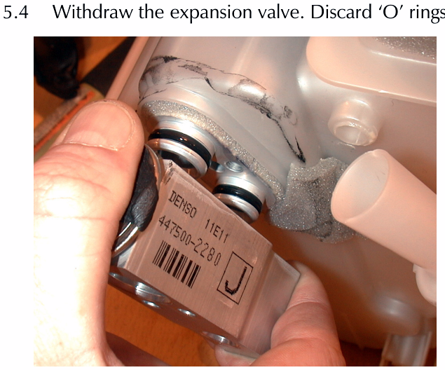 Hands withdrawing the metal expansion valve component, marked DENSO 11E11 447500-2280, from the A/C unit housing.