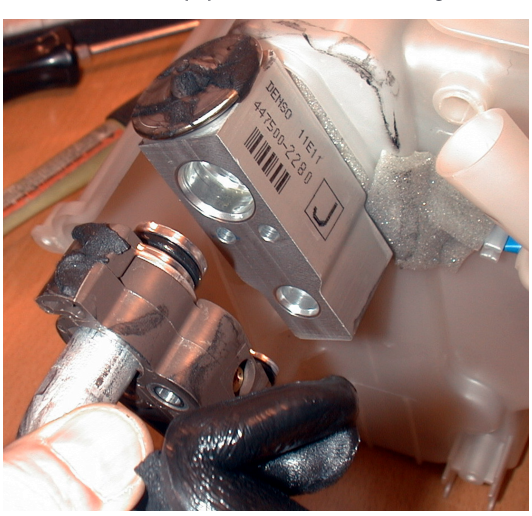 Photo of the expansion valve with A/C pipes removed, held by a gloved hand