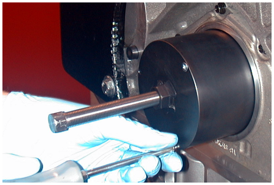 A gloved hand inserting a screw into a black cylindrical oil seal removal tool attached to an engine block.
