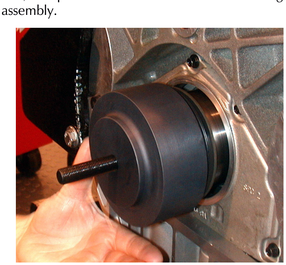 A hand positioning a black cylindrical oil seal install tool against an engine block housing.