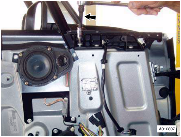 Close-up view of a hand using a tool to remove a bolt from the mirror mounting bracket inside the door panel.