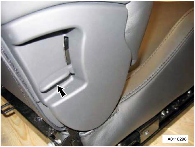 Close-up of a grey car seat showing a black arrow pointing to a release lever on the side panel. The seat has beige leather trim and is mounted on a metal frame.