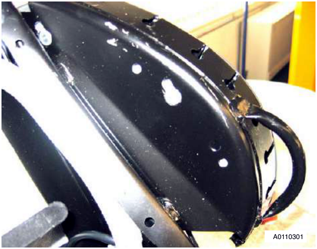 Close-up of a black car seat back shell with visible bolts and mounting points. The shell has white paint residue and is partially disassembled.