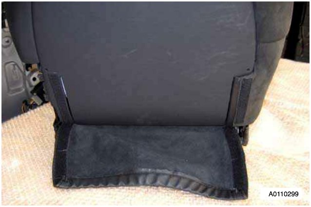 Close-up of a black car seat back shell with a black fabric cover attached by two velcro straps. The cover is partially detached and lies on the floor.