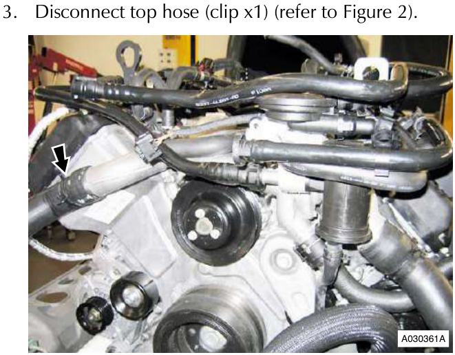 Engine bay showing coolant hoses and components with an arrow pointing to a connection point on the left side of the manifold area.
