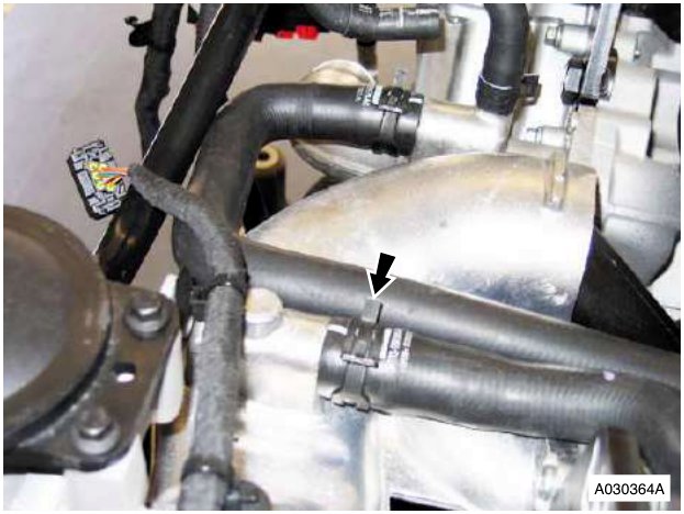 Close-up of black rubber hoses connected to a metal component with an arrow pointing to a clip securing a lower hose