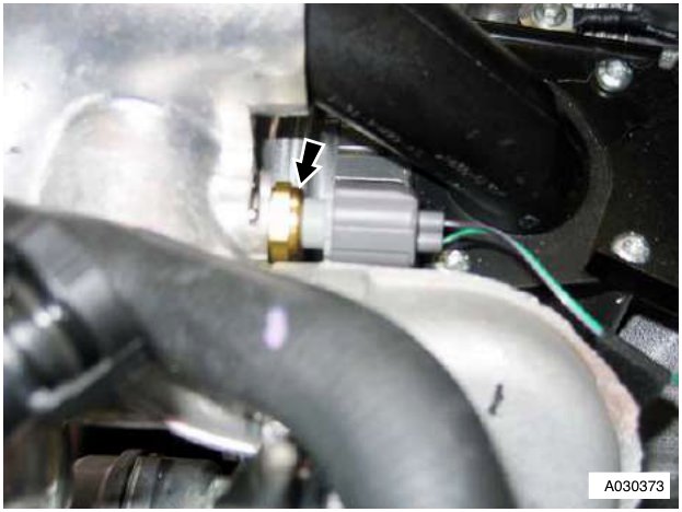 Close-up of a grey electrical multiplug connector attached to a silver metal engine component, with an arrow pointing to the connection point