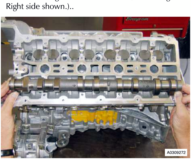 Right side view of engine cylinder head with camshaft being removed, showing hands holding the camshaft and a red Snap-on tool in the background.