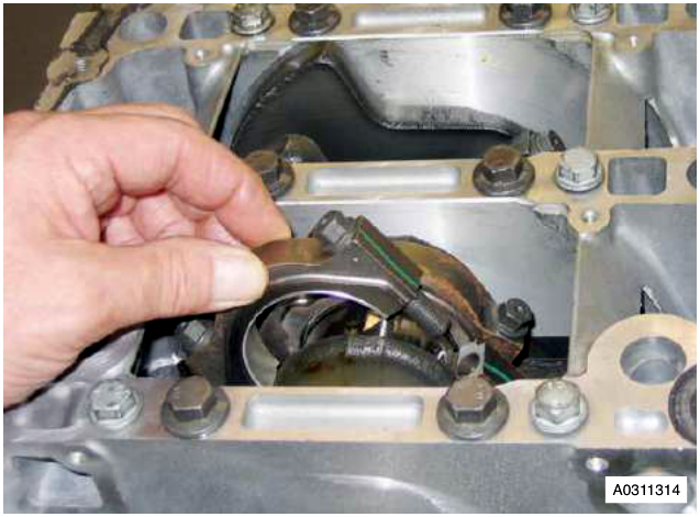 Hand removing a bearing shell from a connecting rod on an engine block.