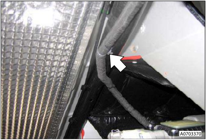 Close-up view of a black rubber hose connected to a metal bracket near a white panel. A red arrow points to the connection point.