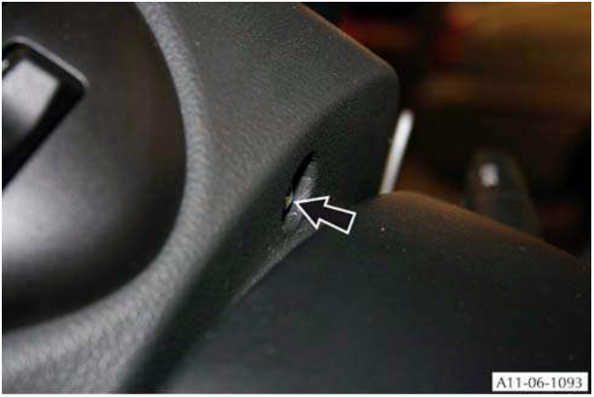 Close-up of a switch on a steering column with an arrow pointing to a small hole or slot.