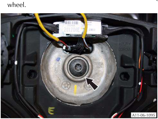 Close-up view of the M10 Torx attachment screw on the steering wheel hub with an arrow pointing to it