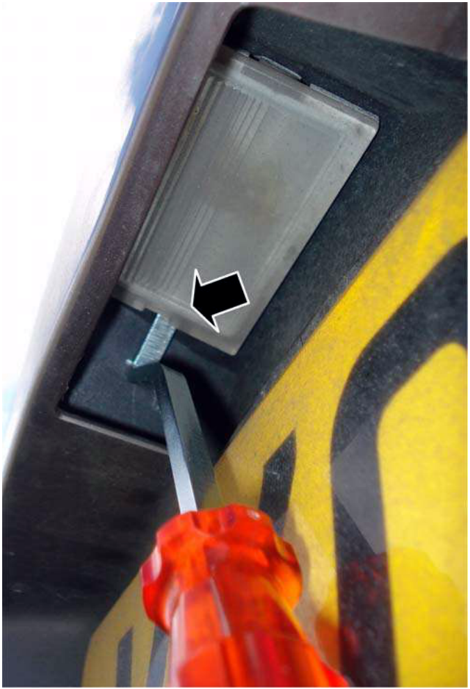 A close-up view showing a tool being inserted between the lamp assembly and the bumper, with an arrow pointing to the insertion point. The background shows part of the car's rear bumper and a yellow warning stripe.