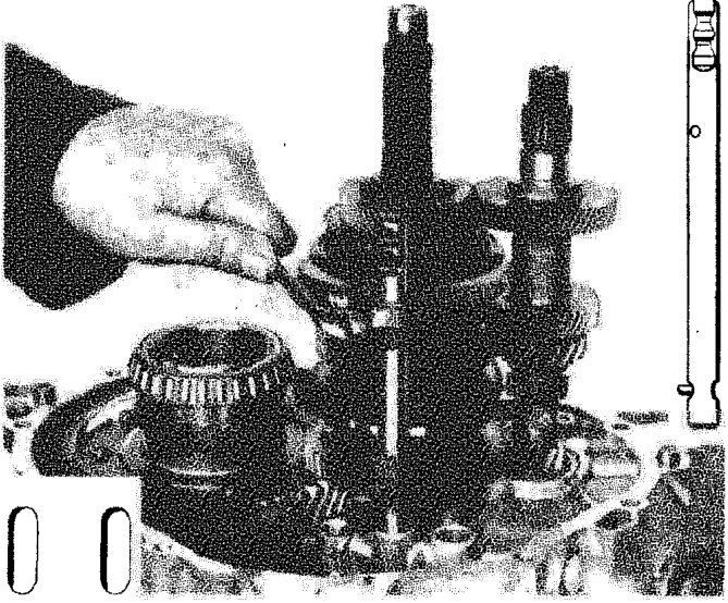 A hand fitting a pin into a rod on the gearbox assembly, with selector forks visible.