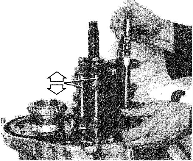 A hand inserting a control rod into the gearbox assembly, with double-headed arrows indicating movement.
