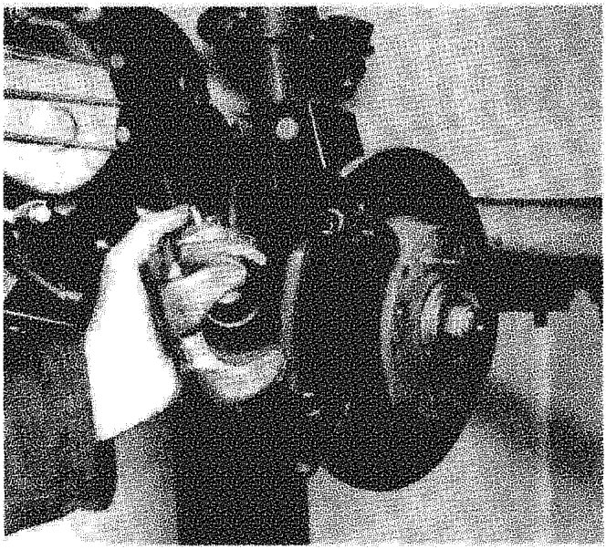 A hand working on the brake caliper assembly attached to the steering knuckle, with the brake disc visible.