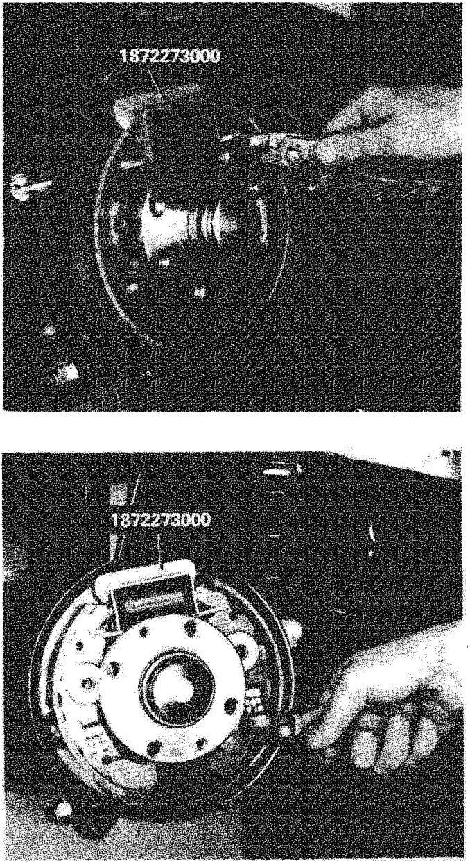 A hand using a tool to remove the upper return spring from the brake shoe assembly