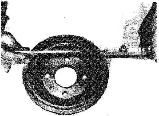 A hand using a measuring tool to check the inside diameter of a rear brake drum mounted on a hub assembly.