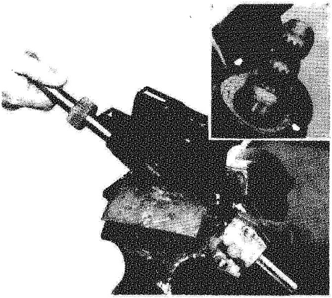 A hand using a tool to work on the upper steering control shaft and bushes secured in a bench mounting; an inset shows a close-up detail of the component.