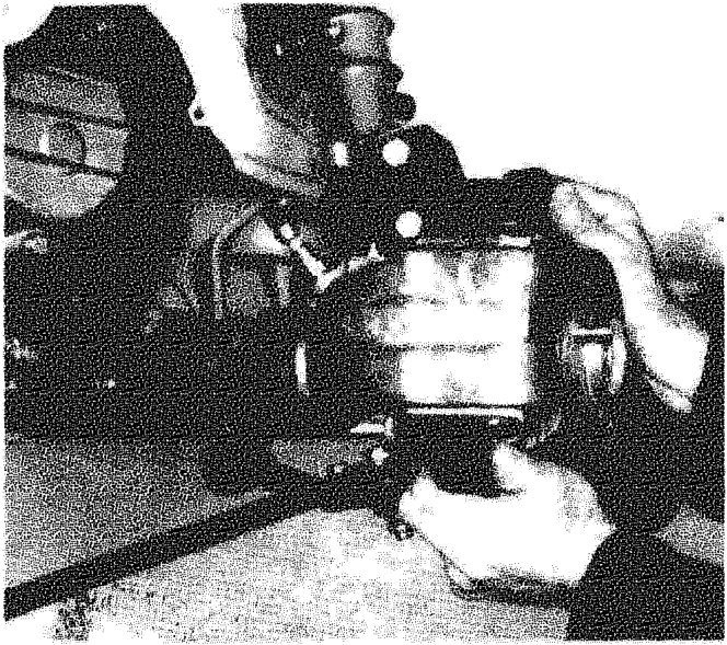 A hand using a tool to remove nuts from the shock absorber assembly turret.