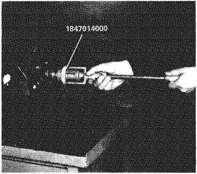 Two hands using a long tool to pull a wheel hub cap (labelled 1847014000) off a shaft.