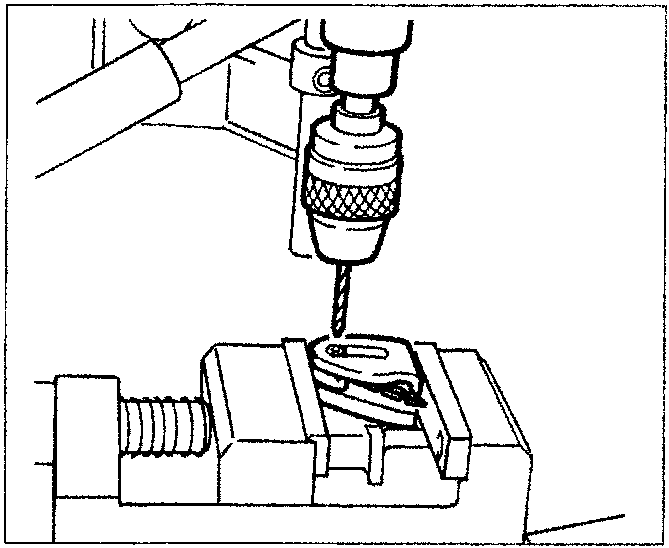 A drill being used to break the shell of a key head that is secured in a clamp