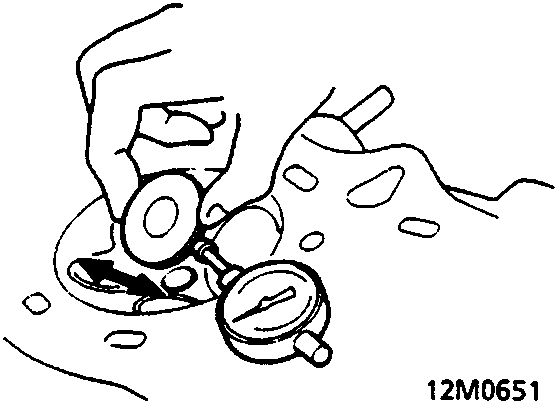 Diagram showing a dial indicator measuring valve stem clearance in the cylinder head