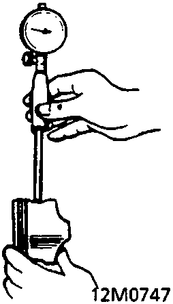 A dial indicator measuring the clearance between a gudgeon pin and a piston (12M0747).